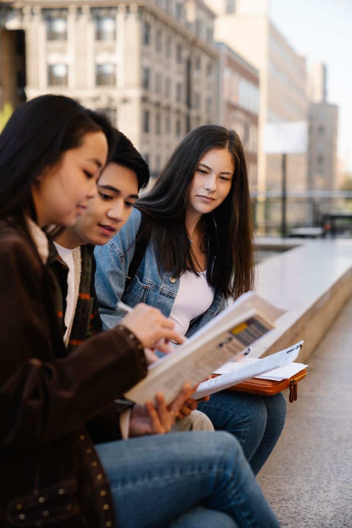 Three students engage in group study on an urban campus bench.