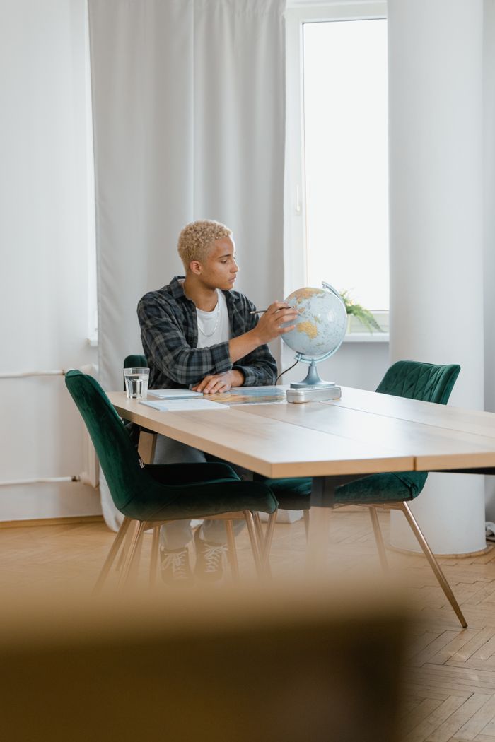 Young adult points at globe while studying indoors at a table, emphasis on education.